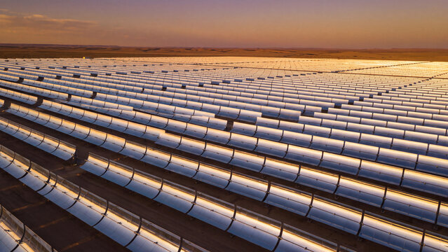 Solar thermal power and renewable energy generation, parabolic trough mirrors arranged in uniform rows across a desert solar farm reflecting golden sunlight for sustainable electricity production
