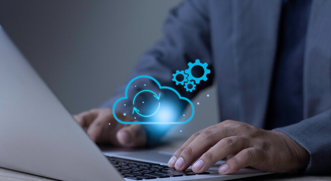 Cloud computing system sync and workflow automation concept with businessman using laptop keyboard displaying glowing sync cloud and gears processing icon on dark background.