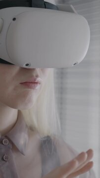 Close-up slow motion of albino girl using virtual reality glasses smiling enjoying gaming device indoors at home. VR gadget and entertainment concept.