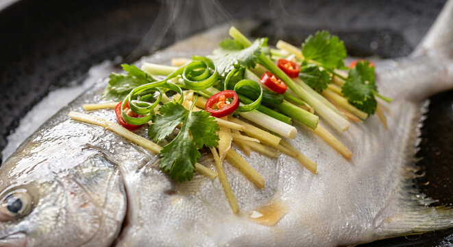 Close-up of whole steamed fish topped with ginger, scallions, cilantro and red chili in aromatic sauce.