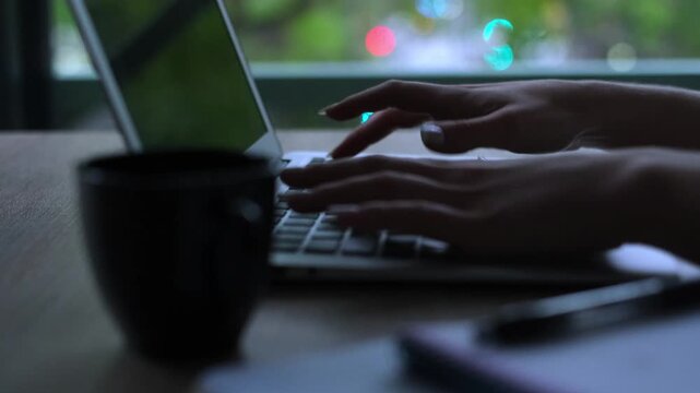 Close up of a woman's hands with a futuristic holographic implant typing on a laptop, representing concepts of ai, data entry, hacking, and advanced human-computer interaction in a dark office