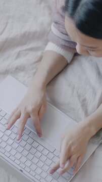Top view slow motion of Asian girl working with laptop in bed typing looking at screen focused on online activity at home. Business and technology concept.