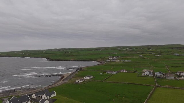 Aerial view of green fields, stone walls, and houses along the rugged coastline under a cloudy sky in Cashel, County Tipperary, Ireland.