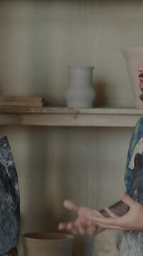 Man and woman in aprons potters talking and looking at ceramics discussing small business in workshop. Creative business and people concept.