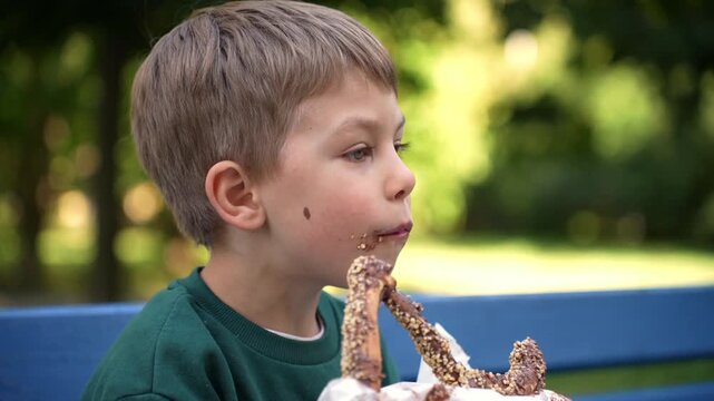 Close-up of a young boy eating a pretzel on a park bench, illustrating childhood enjoyment, casual snacking and outdoor lifestyle.
