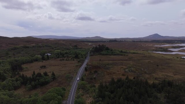 Aerial view of a winding road cutting through the rugged bogland and green forests of Connemara in Galway, County Galway, Ireland.