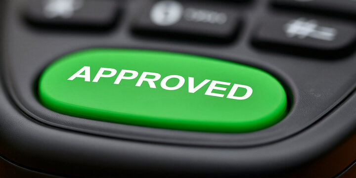 Close-up of a bright green APPROVED button on a dark keypad. The button is illuminated, signifying a positive confirmation or selection.