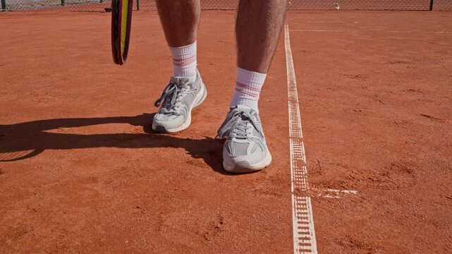 Caucasian young adult man bouncing tennis ball on clay court while holding racket. Clip ideal for tennis coaching apps and athletic footwear commercial campaigns
