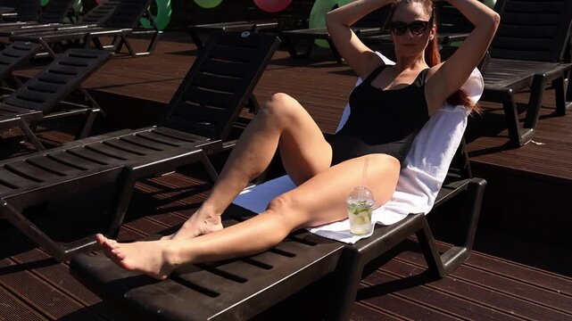 Woman relaxing on a lounge chair outdoors, mid-stretch pose, leisure time, vacation vibe.