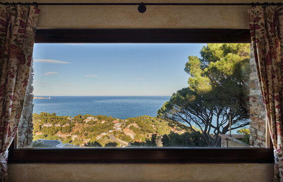 Scenic ocean view through interior window with foreground tree, coastal hills, calm horizon, and clear blue sky creating peaceful seaside composition, with ocean, window, view, coast detail
