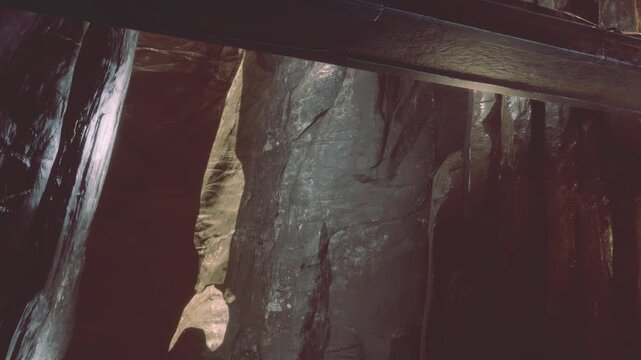 The scene shows the interior of a cave featuring large rock formations. A wooden beam supports the structure above. The lighting creates shadows that add depth to the cave.