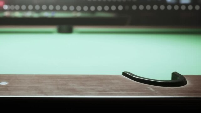 A pool table is shown in detail, focusing on the wooden edge and green felt. The scene is set in a game room with players present in the background. It is evening time.