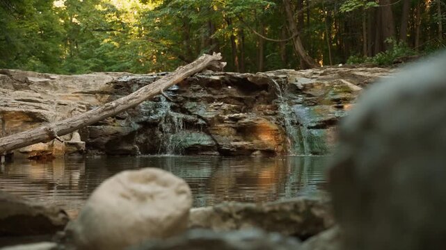 Cinematic rack focus from a foreground river rock to a picturesque forest waterfall in Seneca Falls NY