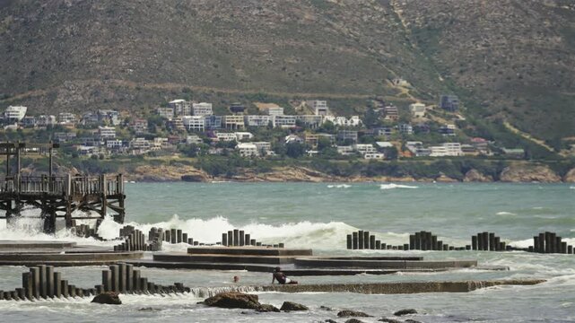 local kids swimming and play in tidal pool with crashing waves against mountain seaside homes