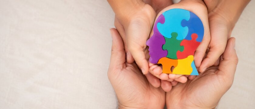 hands holding colorful puzzle shaped human head representing autism awareness, neurodiversity, developmental support and inclusion