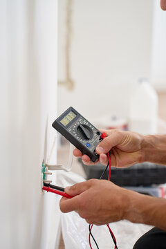 Electrician testing wall socket voltage with digital multimeter