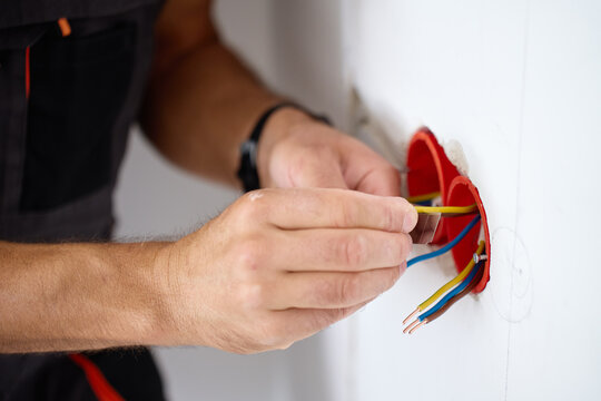 Hands working with electrical wires inside a wall