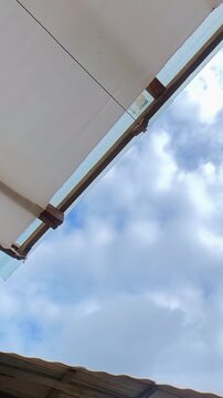 Timelapse of clouds moving across a blue sky, viewed from beneath a rooftop with a simple architectural frame.