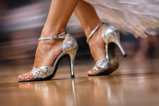 Closeup shows metallic sandal heels stepping confidently across wooden dance floor