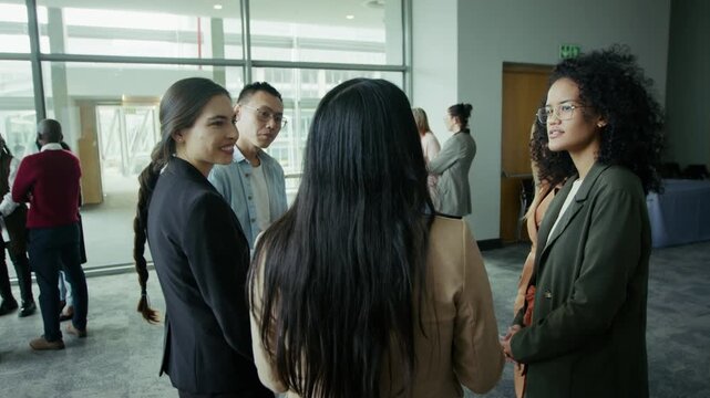 Diverse business professionals engage in conversation and networking at a conference or corporate event. They are seen discussing and interacting in a large, open venue.
