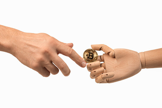 Human hand reaching for bitcoin held by wooden robotic hand. Artificial intelligence, cryptocurrency, blockchain, fintech, automation and future digital finance concept.