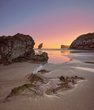 Wet sand, rocks, tidal pools, 'El Pic&oacute;n' limestone p&igrave;nnacle, Playa de Buelna Beach at low tide on a spectacular, fiery dawn. Llanes-Asturias-Spain-079