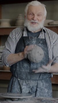 Portrait of senior man working with clay in studio and talking looking at camera recording video about pottery for social media vlog. Small business and vlogging concept.