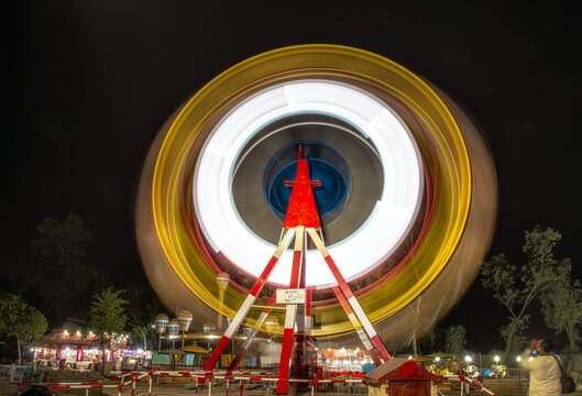 View of a brightly illuminated Ferris wheel captured with a long exposure effect creating vibrant light trails at an amusement park in Lahore, Punjab, Pakistan.