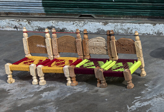 View of miniature wooden handicraft toys featuring intricate carvings and colorful woven seats arranged on a concrete surface in Charbagh, Khyber Pakhtunkhwa, Pakistan.