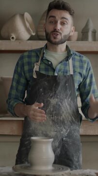 Slow motion portrait of professional potter recording video in workshop talking about pottery and looking at camera. creative man wearing dirty apron.