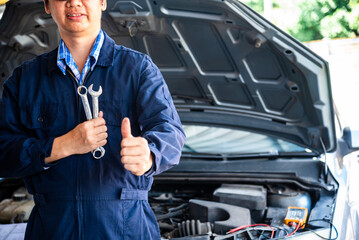 Close up Mechanic man hands repairing car auto repair shop uses jack change tyre. Open vehicle hood...