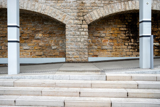 Stone wall with arched recesses stands behind white columns and steps where masonry architecture meets a clean empty urban public space