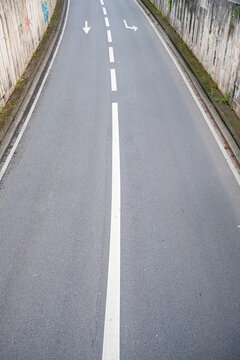 Empty asphalt road with a white center line stretches through an urban corridor where simple markings and perspective create a minimal transportation scene