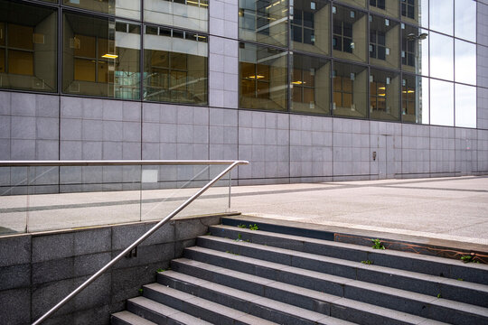 Modern building entrance with steps and a metal handrail forms a clean urban exterior where glass windows and stone surfaces frame an empty architectural space