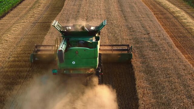 Rear aerial view of a combine harvester trailing dust in a field