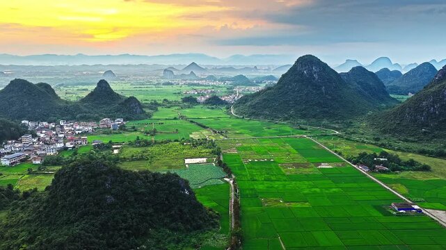 Aerial view of karst mountains and rural village with rice paddies at sunset in Guilin, China.