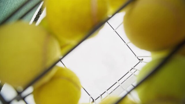 Young adult Caucasian man taking tennis balls from hopper in POV shot. Useful for tennis academy marketing, athletic training commercials, and sport coaching content