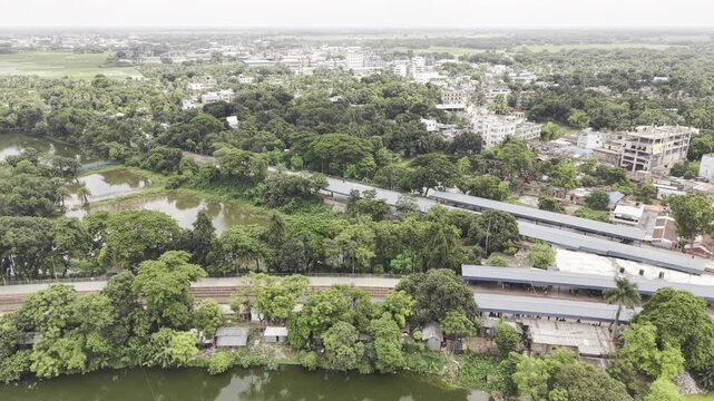 Rightward-moving aerial drone footage over Poradaha Junction Railway Station in Bangladesh, showing railway platforms, multiple tracks, station buildings, greenery, and the surrounding landscape.