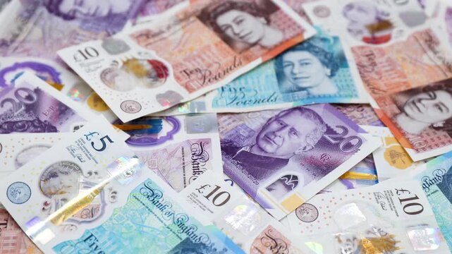 Heap of British pound banknotes with portraits of Queen Elizabeth II and King Charles III.