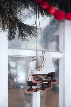 White ice skates hanging from a window with red ornaments and pine branches, creating a festive winter decoration in a cozy indoor setting