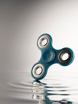 Blue fidget spinner creating ripples on calm water surface, a symbol of focus