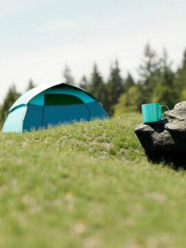 A turquoise camping tent set up on a grassy hill with a mug on a rock