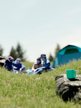 Friends enjoying a sunny day camping with a tent and a mug in the foreground