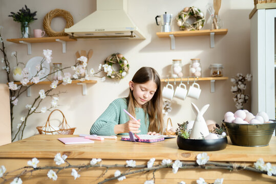 Cute Little Girl Drawing in Her Notebook in Easter Decorated Kitchen