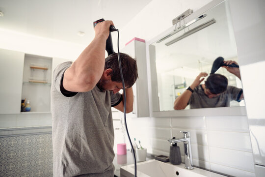 Man drying his hair with a hairdryer in front of a bathroom mirror