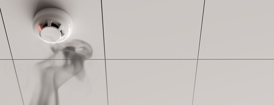 Smoke detector on a white tiled ceiling with a faint red light and wisps of smoke