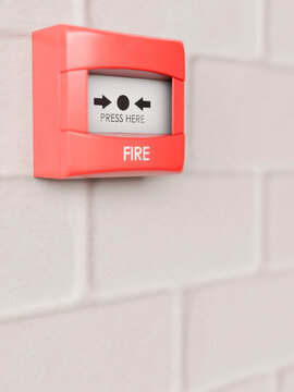 Red fire alarm pull station mounted on a white brick wall for emergencies