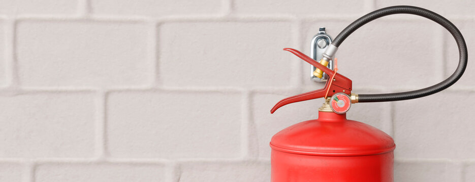 Red fire extinguisher mounted on a white brick wall, ready for emergencies