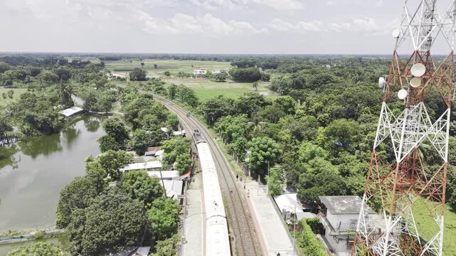 12 August 2026, Kushtia, Bangladesh: Aerial footage of a passenger train departing Poradah Junction in Kushtia, Bangladesh, with parallel railway tracks, station platforms, lush vegetation, and ponds.