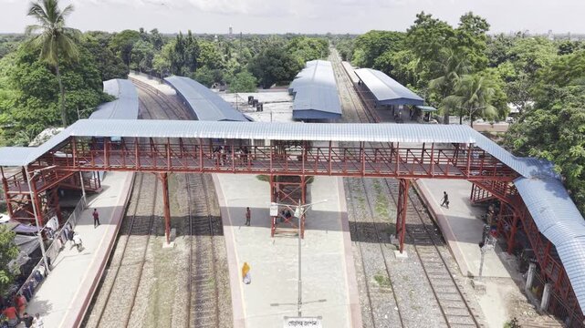 Aerial drone footage captures a cargo train arriving at Poradah Junction in Kushtia, Bangladesh, with railway platforms and tracks surrounded by green vegetation, ponds, rural homes, and farmland.